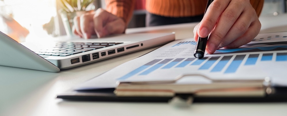 Business Documents On Office Desk With Laptop And Smart Phone And Graph Business Diagram And Women Working At Office .