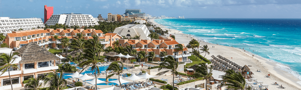 large resort property surrounding swimming pools and palm trees that stretch to a white sand beach and turquoise sea with resorts in the distance